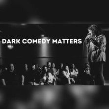 Ein Comedian steht auf einer Bühne vor einem Publikum. Der Text 'Dark Comedy Matters' ist im Bild zu sehen.