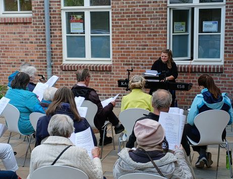 Menschen sitzen draußen vor dem Kulturzentrum und singen gemeinsam