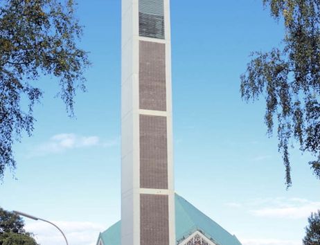 Moderne Kirche mit hohem Glockenturm und grünem Dach, umgeben von Bäumen.