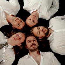 Fünf Personen in weißen Hemden liegen im Kreis mit den Köpfen zusammen.