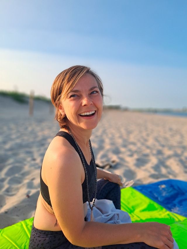 Frau sitzt lächelnd auf einer bunten Decke am Strand.