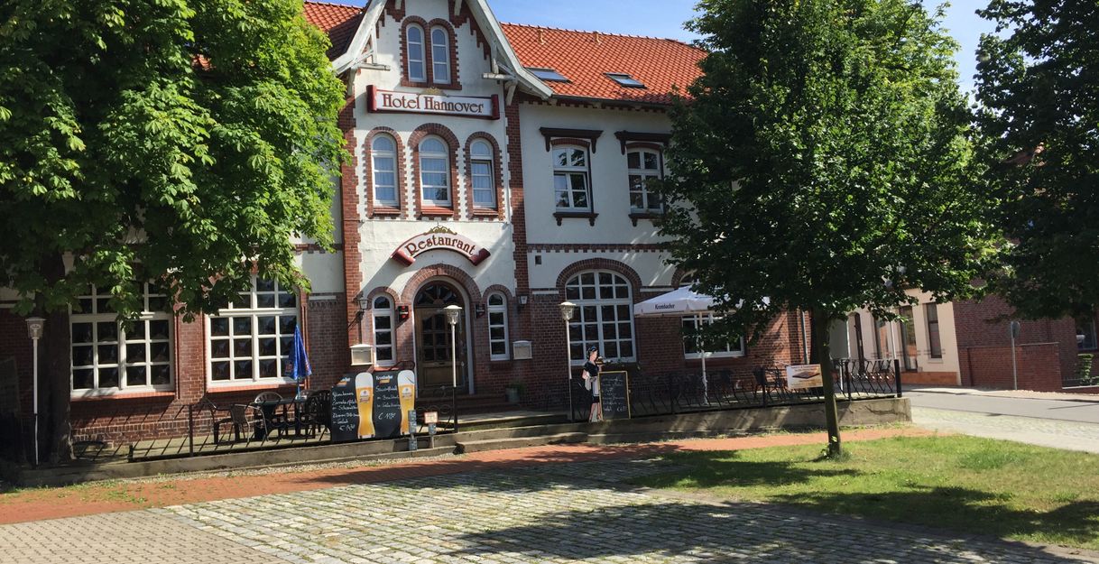 Historisches Gebäude mit der Aufschrift 'Hotel Hannover' und 'Restaurant', umgeben von Bäumen.