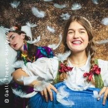 Zwei Frauen in einem Theaterstück, umgeben von Federn. Eine Frau lächelt, während die andere schläft.