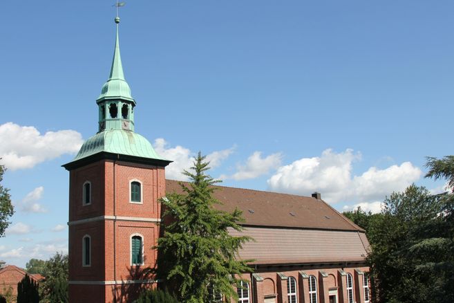 Kirche St. Pankratius in Ochsenwerder mit rotem Backsteinturm und grünem Dach vor blauem Himmel.