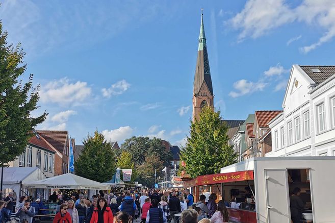 Menschenmenge auf einem Stadtfest mit Essensständen und einer Kirche im Hintergrund.