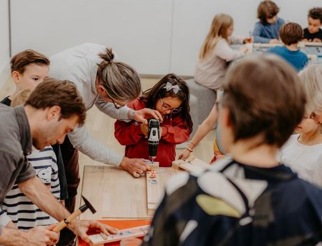 Kinder und Erwachsene arbeiten gemeinsam an einem Holztisch mit Werkzeugen.