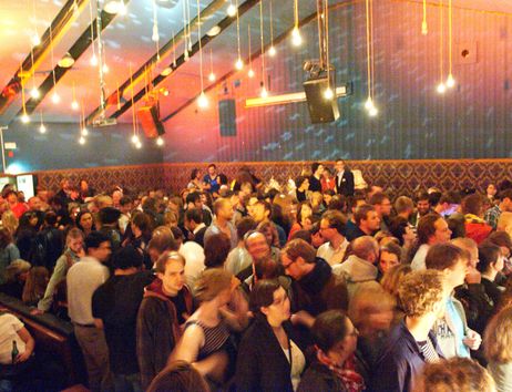 Menschenmenge in einer Bar mit hängenden Glühbirnen.