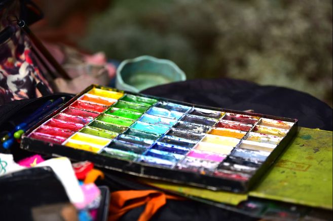 Eine bunte Palette mit verschiedenen Farben und Pinseln auf einem Tisch in einer kreativen Werkstatt.
