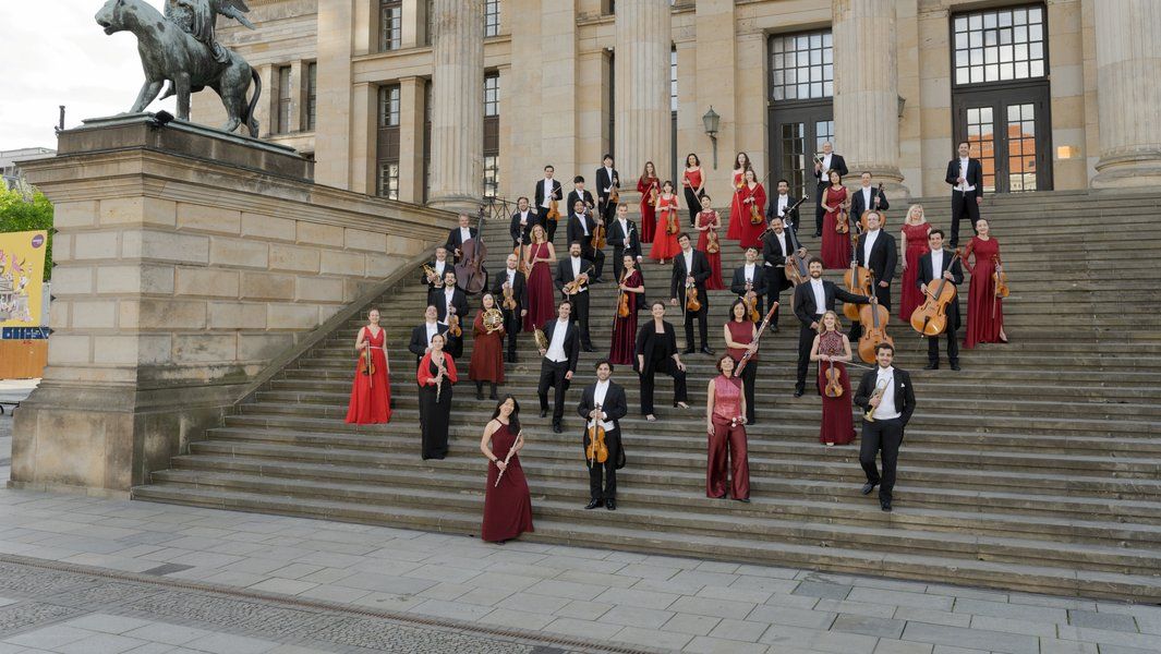 Eine Gruppe von Musikern in formeller Kleidung steht auf einer breiten Treppe vor einem historischen Gebäude.