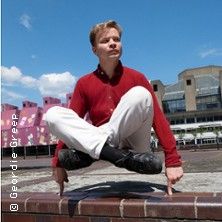 Person in rotem Hemd und weißer Hose balanciert auf einer Mauer vor einem modernen Gebäude.