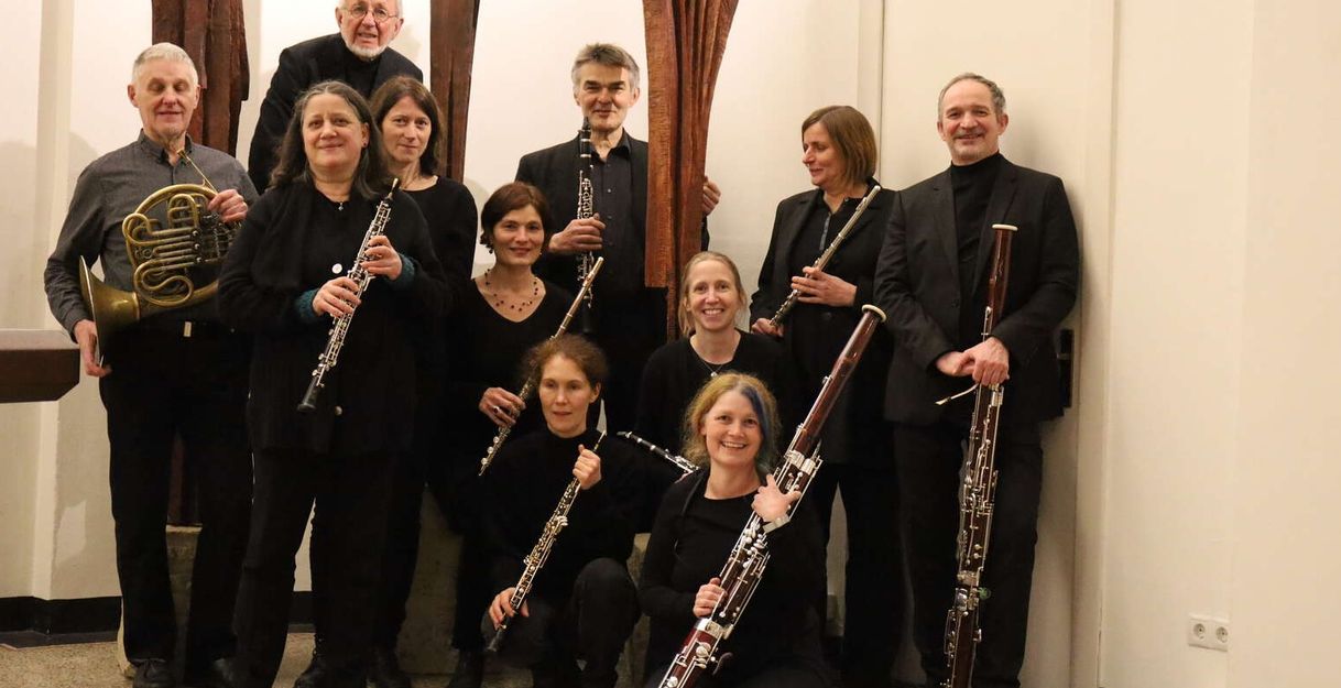 Eine Gruppe von Musikern mit Blasinstrumenten posiert in einem Innenraum.