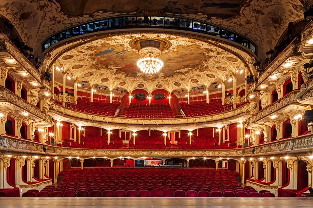 Das Saal des Deutschen SchauSpielHauses aus Sicht der Bühne: Rot bezogene Samt-Sitze und goldener Stuck, in der Mitte der Decke der große Kronleuchter.