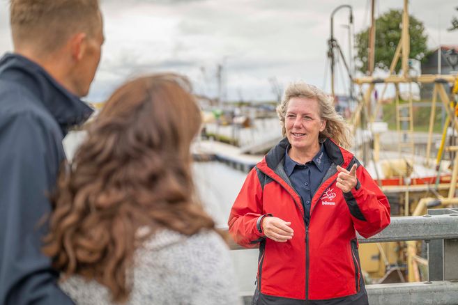Eine Frau in roter Jacke spricht mit zwei Personen am Hafen von Büsum.