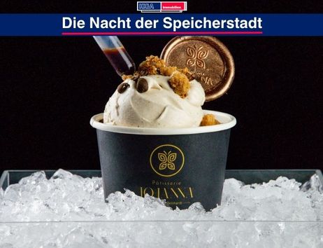 Ein Becher Eiscreme von Patisserie Johanna auf Eiswürfeln, dekoriert mit Schokolade und Keksstücken, mit einer Spritze für Sirup.