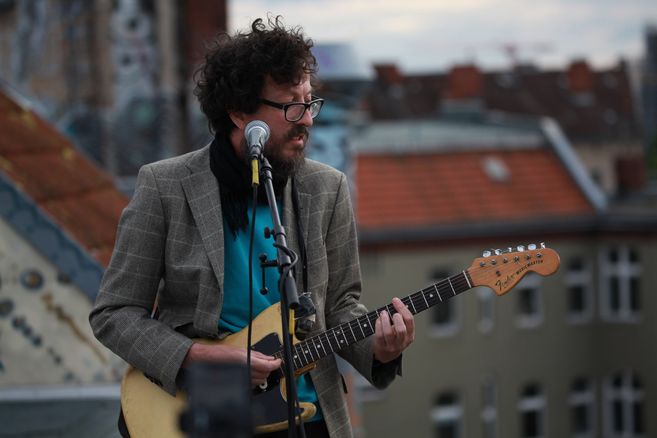 Musiker mit Gitarre auf einem Dachgeschoss vor seinem Mikrofon