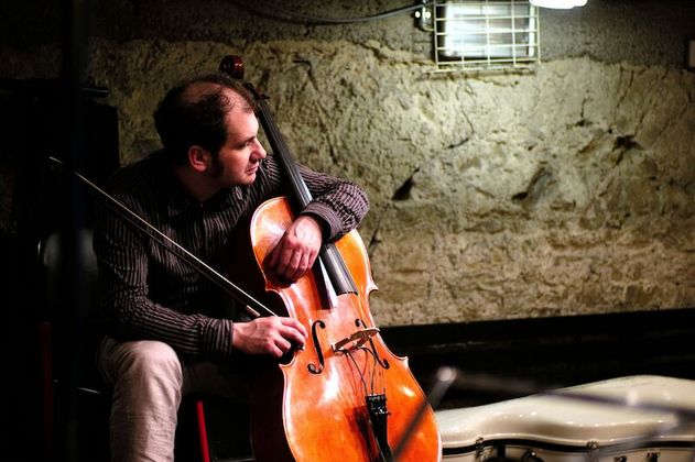 Ein Mann spielt Cello in einem Raum mit Steinwänden.