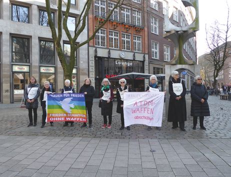 Frauen in Schwarz bei einer Mahnwache mit Bannern gegen Atomwaffen auf einem Platz.