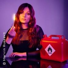 Eine Frau hält ein brennendes Streichholz neben einem roten Kanister mit Flammensymbol.