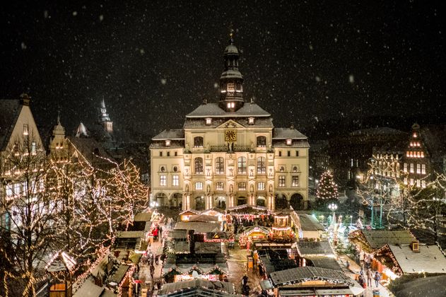 Weihnachtsmarkt in Lüneburg bei Nacht mit beleuchtetem Rathaus und schneebedeckten Ständen.