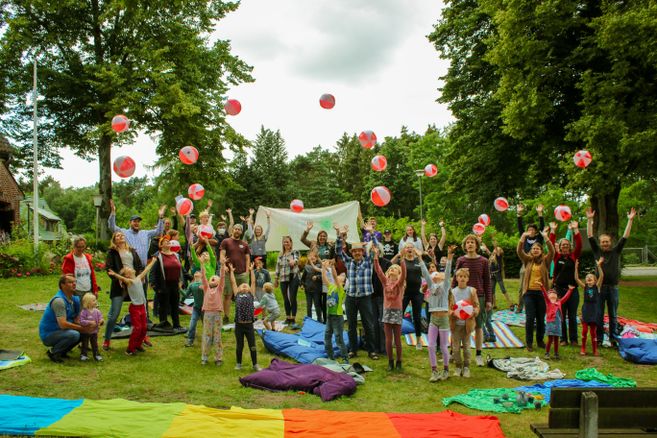 Eine Gruppe von Menschen wirft bunte Strandbälle in die Luft in einem Park.