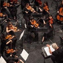 Ein Orchester spielt ein Symphoniekonzert, dirigiert von einem Dirigenten. Die Musiker spielen Streichinstrumente.