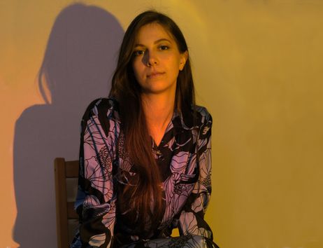 Eine Frau sitzt in einem Stuhl, beleuchtet von warmem Licht, das Schatten an die Wand wirft.