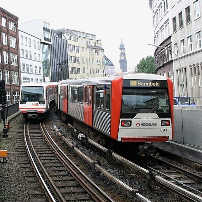 Zwei U-Bahn-Züge der Hamburger Hochbahn auf parallelen Gleisen in der Stadt.