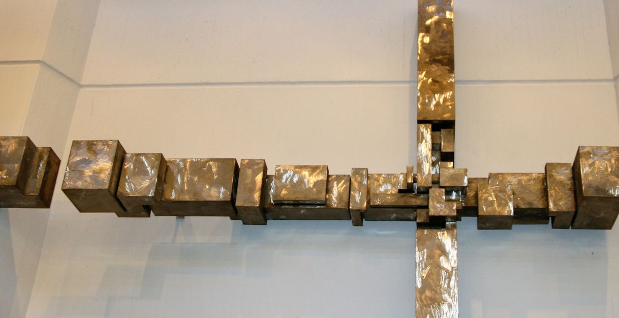 Metallskulptur eines Kreuzes an einer Wand.