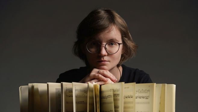 Person mit Brille blickt ernsthaft über ein aufgeschlagenes Notenbuch.