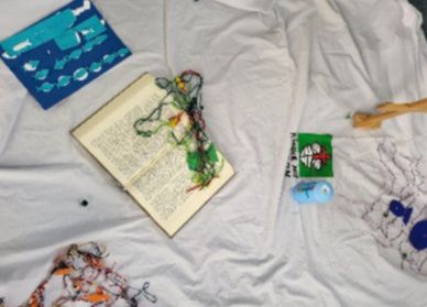 Ein aufgeschlagenes Buch liegt auf einem weißen Tuch, umgeben von bunten Bastelmaterialien und Zeichnungen.