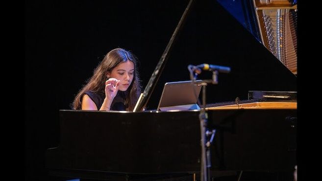 Eine Frau spielt konzentriert Klavier auf einer Bühne.