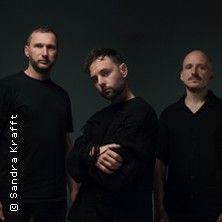 Drei Männer in schwarzer Kleidung vor dunklem Hintergrund.