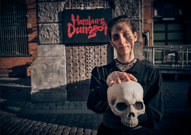 Geschminkte Schauspielerin steht vor dem Hamburg Dungeon Logo