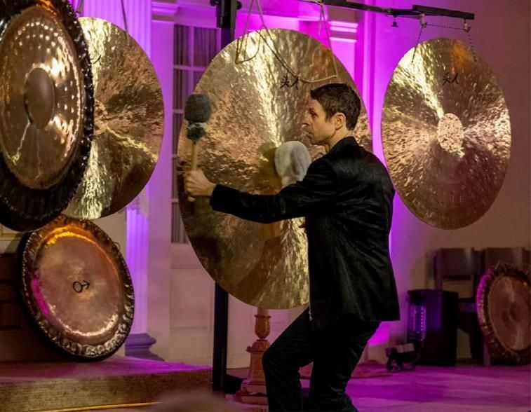 Ein Musiker spielt auf großen Gongs in einem Konzertsaal mit violetter Beleuchtung.