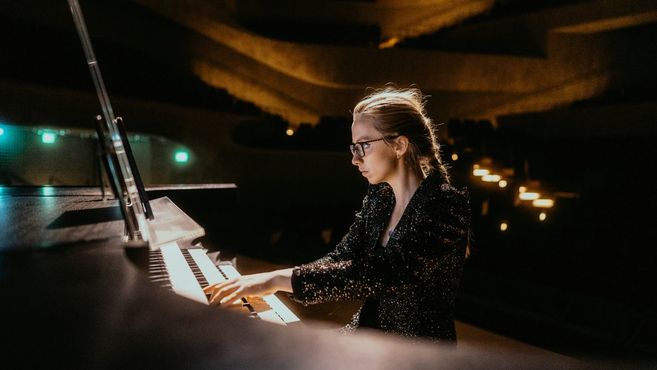 Eine Frau spielt konzentriert Orgel in einem gedämpft beleuchteten Konzertsaal.