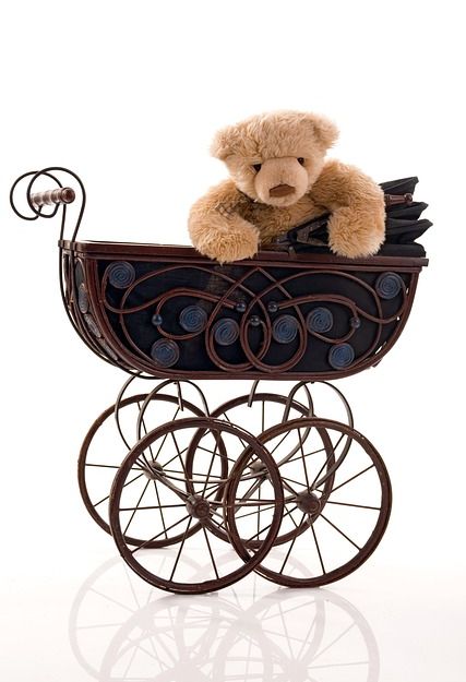 Ein Teddybär sitzt in einem dekorativen, antiken Kinderwagen.