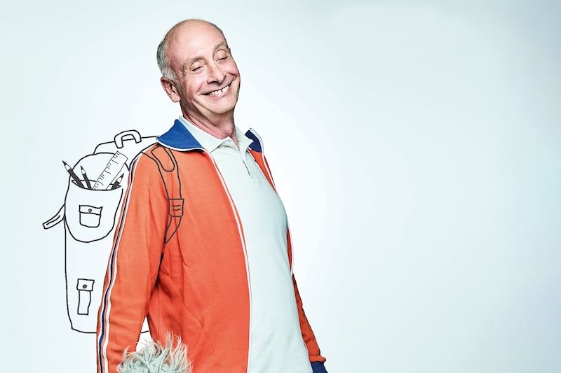 Ein lächelnder Mann in einem orangefarbenen Trainingsanzug mit einer gezeichneten Schultasche im Hintergrund.