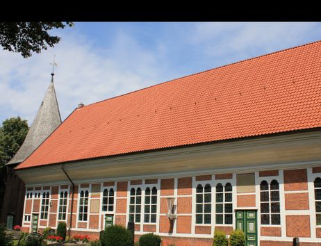 Außenansicht der Dreieinigkeitskirche Allermöhe mit rotem Ziegeldach und Fachwerkfassade.