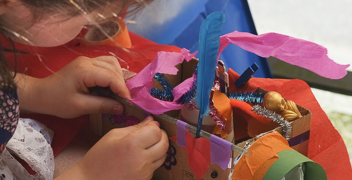 Kind bastelt ein buntes Modell aus Pappe und Papier.