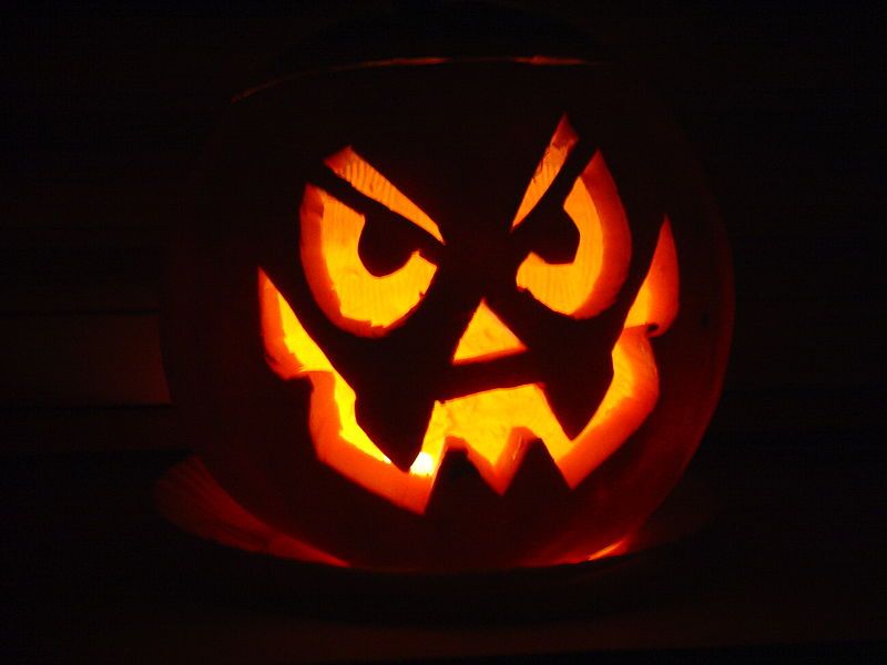 Ein beleuchteter Kürbis mit grimmigem Gesicht, typisch für Halloween.