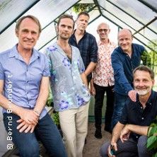 Eine Gruppe von sechs Männern posiert in einem Gewächshaus.