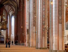 Innenansicht einer gotischen Kirche mit hohen Säulen und Wandmalereien.