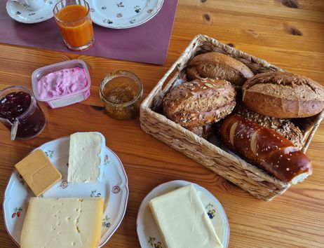Frühstückstisch mit Brötchen, Käse, Marmelade und Saft.