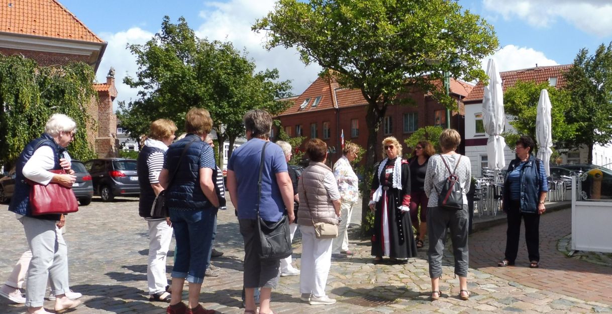 Gruppe von Menschen bei einer Stadtführung in Wesselburen auf einem gepflasterten Platz.
