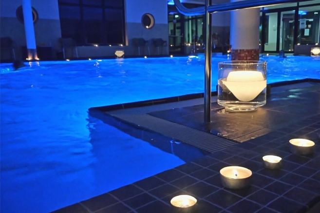 Innenpool im Watt'n Bad mit blau beleuchtetem Wasser und mehreren Kerzen am Beckenrand.