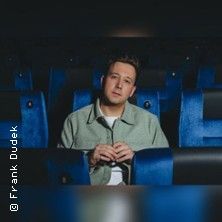 Ein Mann sitzt in einem leeren Kinosaal auf einem blauen Sitz.