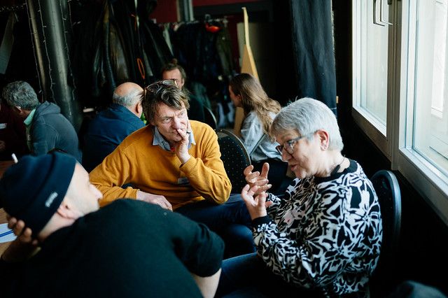 drei Menschen sitzen ins Gespräch vertieft im Kreis und hören einander zu, während eine Person spricht