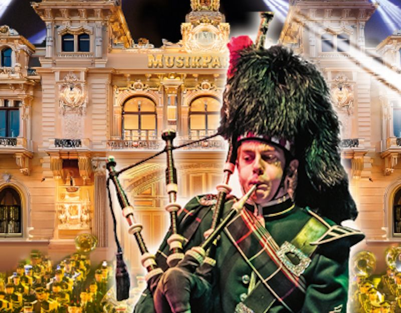 Ein Dudelsackspieler in traditioneller Uniform spielt vor einem beleuchteten Gebäude mit der Aufschrift 'Musikparade'.