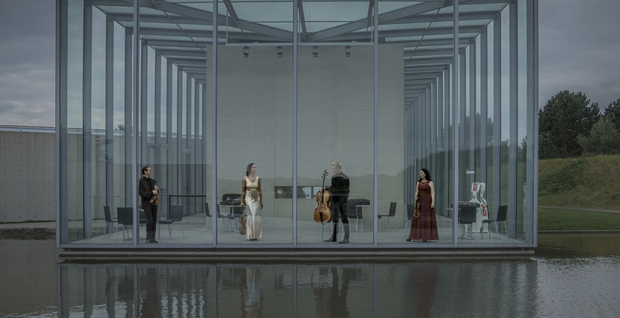 Vier Musiker:innen vom Minguett Quartett stehen auf einer Bühne mit moderner Stahlstrelenkonstruktion am See mit Abendrobe un dihren Streichinstrumenten in der Hand